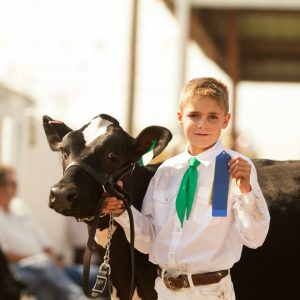 2025 Livestock Shows -boy holding blue ribbon with cow